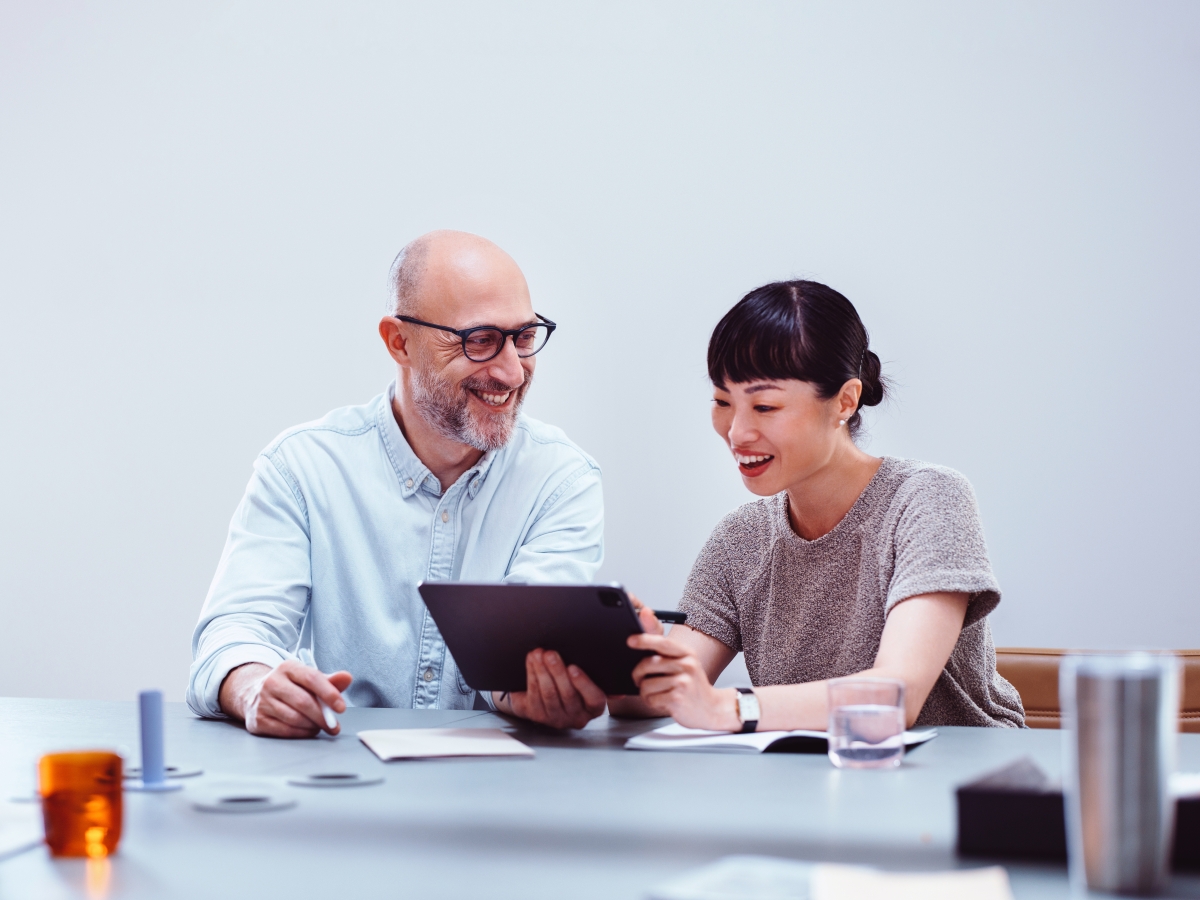 Two people sitting at a table using a tablet.