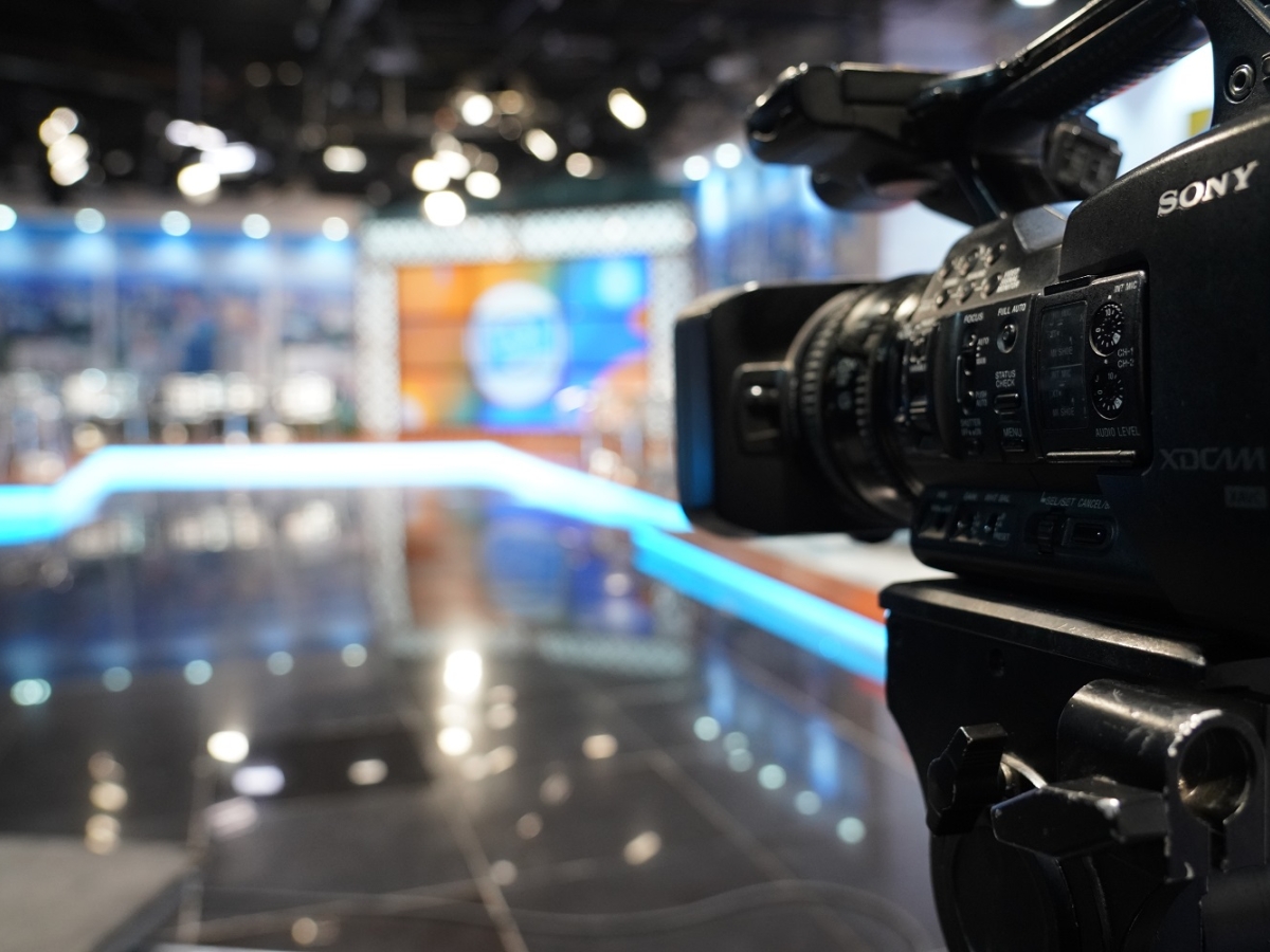 Broadcast camera with lights and a blurred set in the background.