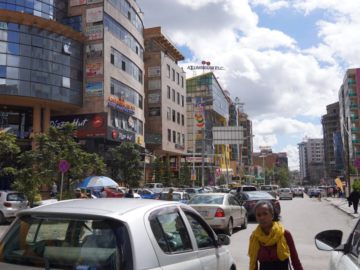 Busy city street with cars, pedestrians, and commercial buildings.