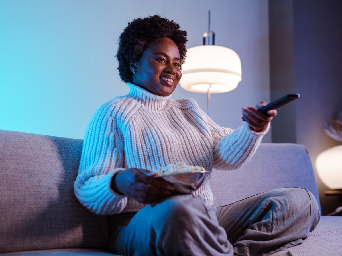 Woman sitting on a couch with popcorn watching television.