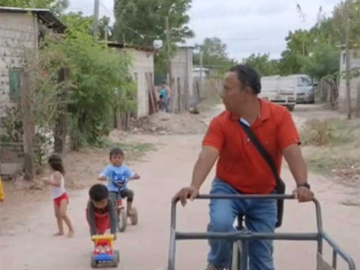 Person riding a bicycle cart with children playing nearby.
