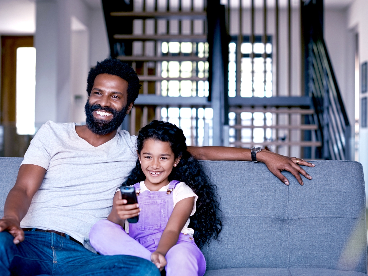 Image of a father and daughter sitting on couch watching television