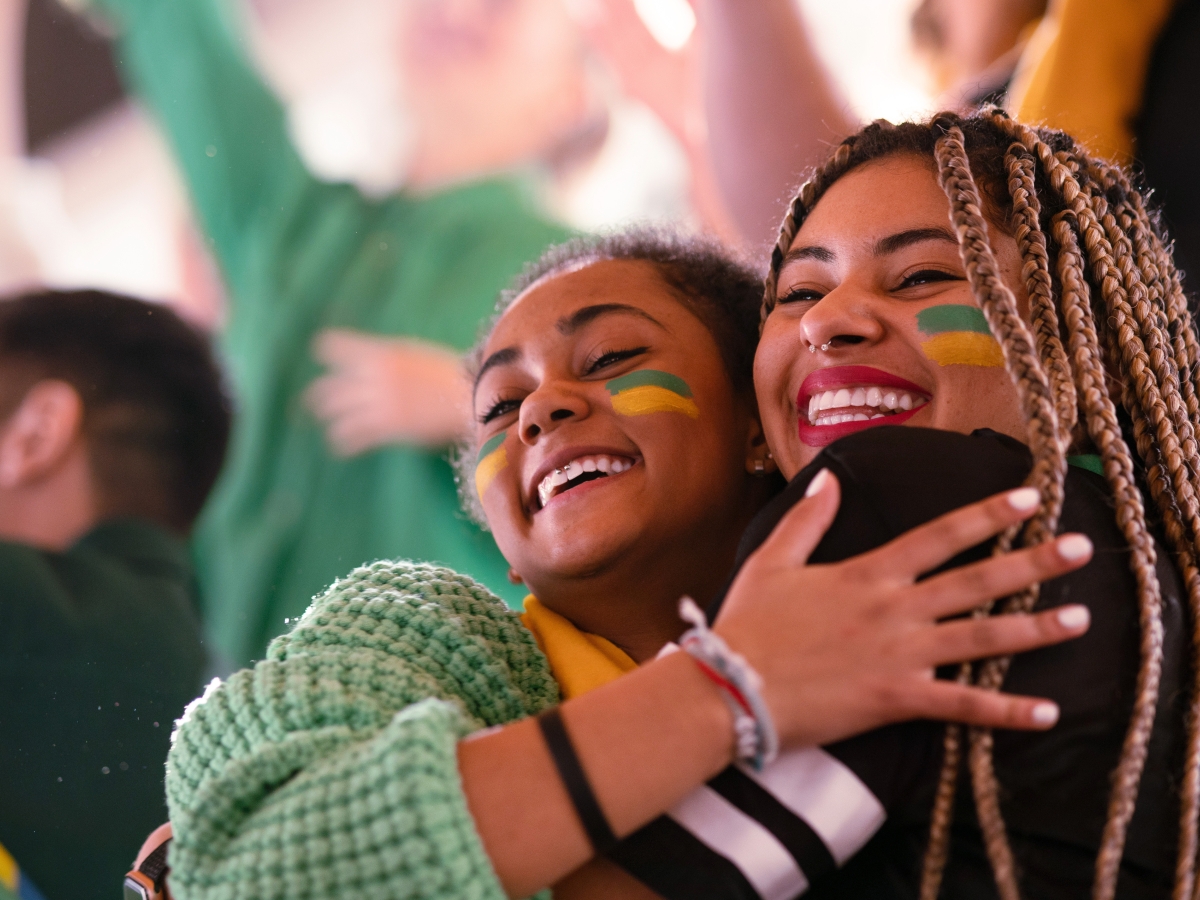 People embracing at a sporting event, with team colors painted on their faces.