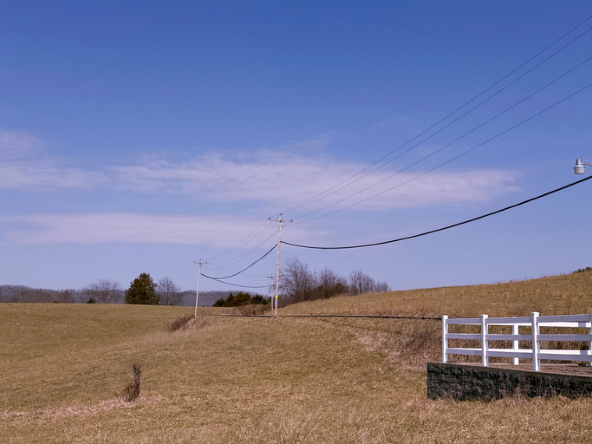 Image of power lines crossing a rural field under a clear sky.