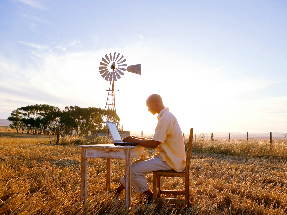 Image of a person using a laptop in a rural landscape.